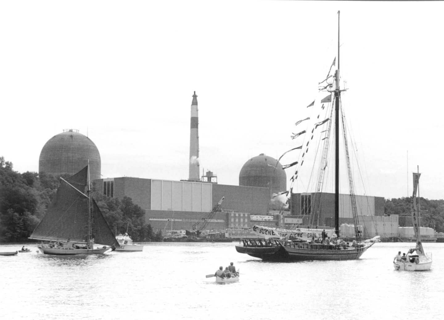 A black-and-white photo of the Sloop Clearwater in front of the Indian Point power station.