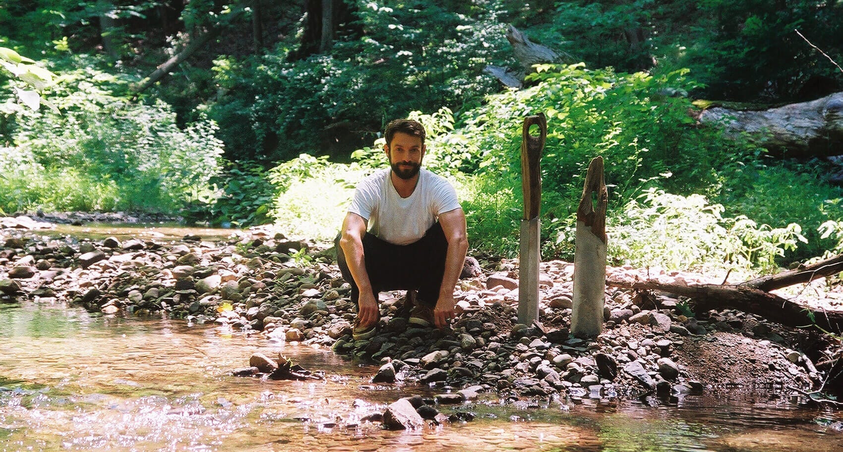 Brad Teasdale crouching by two of his mermaid totem sculptures