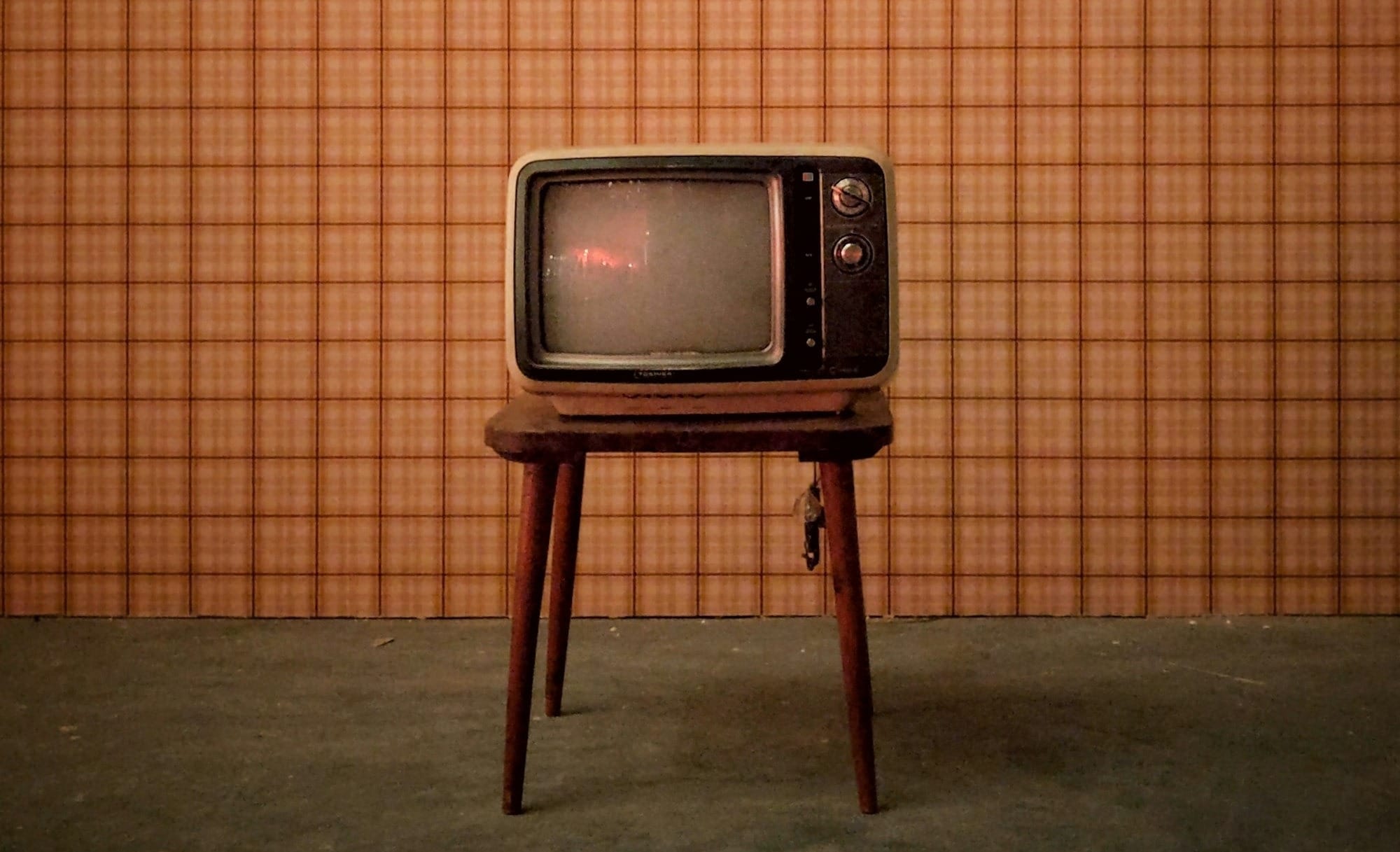 An old-fashioned TV in front of old-fashioned wallpaper